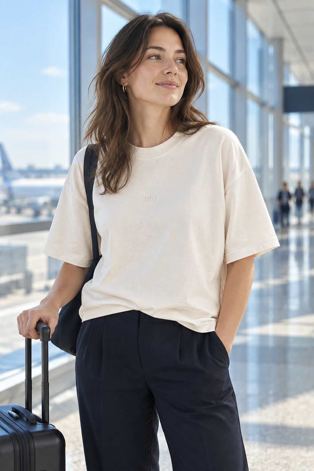 A traveler wearing the Bone Everywhere Tee beside a carry-on in an airport; design concept